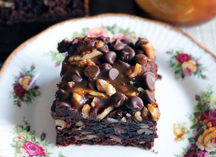 A slice of salted caramel chocolate cake with chocolate frosting and pecan and walnuts.