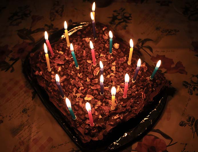 Lit birthday candles on top of the salted caramel chocolate cake with chocolate frosting topped with nuts and more caramel