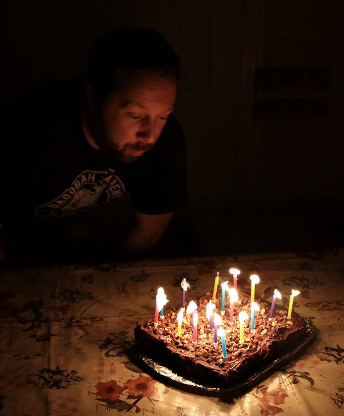 A man blowing out the birthday candles on the salted caramel chocolate cake with chocolate frosting and pecan and walnuts. Salted Caramel Chocolate Cake Recipe