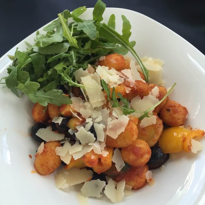 A plate of gnocchi and vegetables covered in Parmesan cheese which is not vegetarian friendly