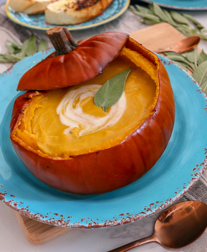 Pumpkin Soup Recipe served in a pumpkin shell garnished with cheese, cream and herbs.