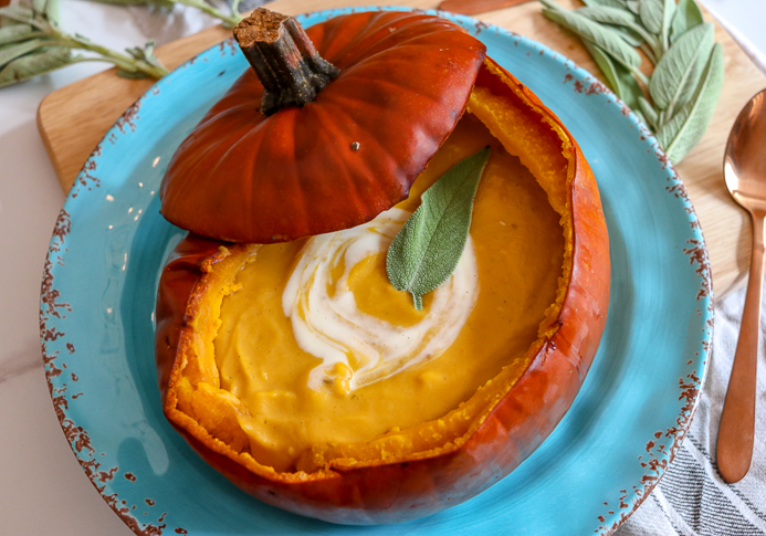 Pumpkin Soup Recipe served in a pumpkin shell garnished with cream and herbs.