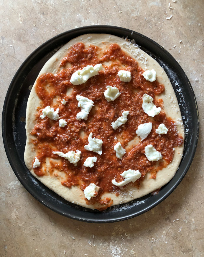 uncooked pizza on a tray waiting to go into the oven